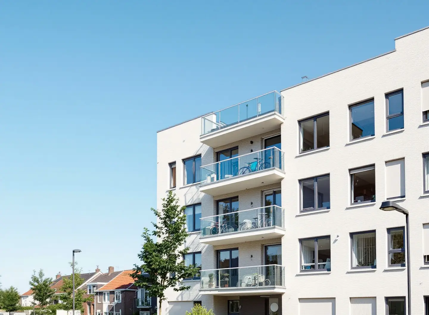 Een gerenoveerd appartementengebouw met een lichte geïsoleerde gevel, nieuwe donkere kozijnen en glazen balkons onder een blauwe lucht